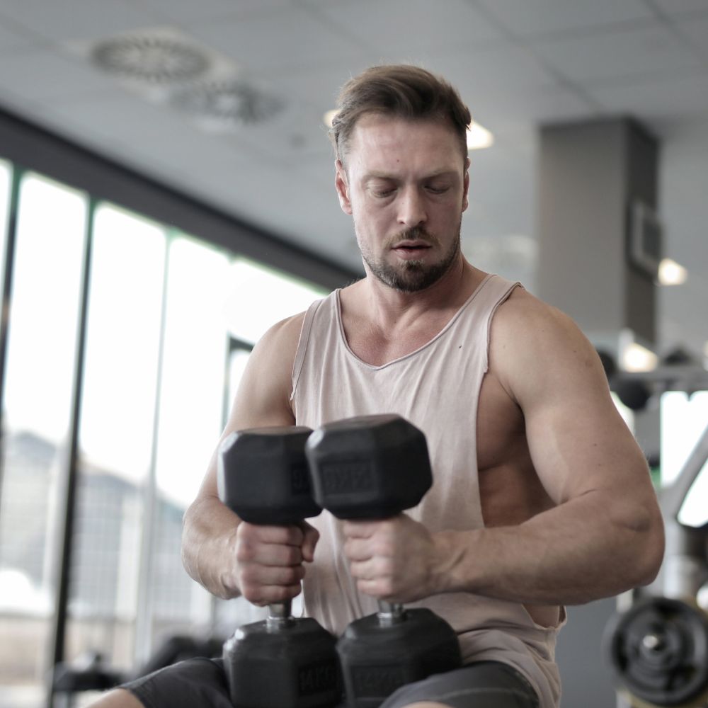 Man lifting dumbbells in gym for muscle strength, recovery, and fitness support